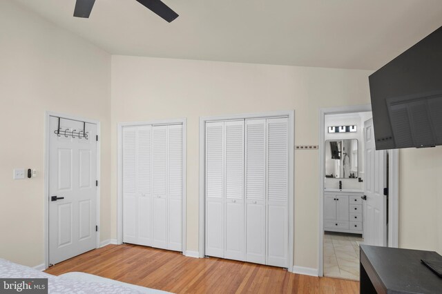 bedroom with vaulted ceiling, light wood-style flooring, ensuite bathroom, and two closets