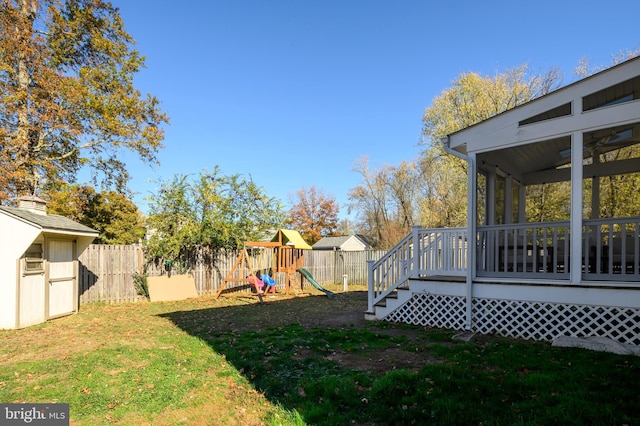 view of yard featuring an outbuilding, a fenced backyard, a playground, a storage shed, and a sunroom