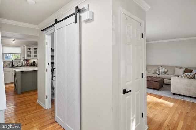 hall featuring a sink, a barn door, light wood-style flooring, and ornamental molding