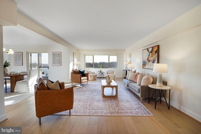 living area with a wealth of natural light, baseboards, wood-type flooring, and a chandelier