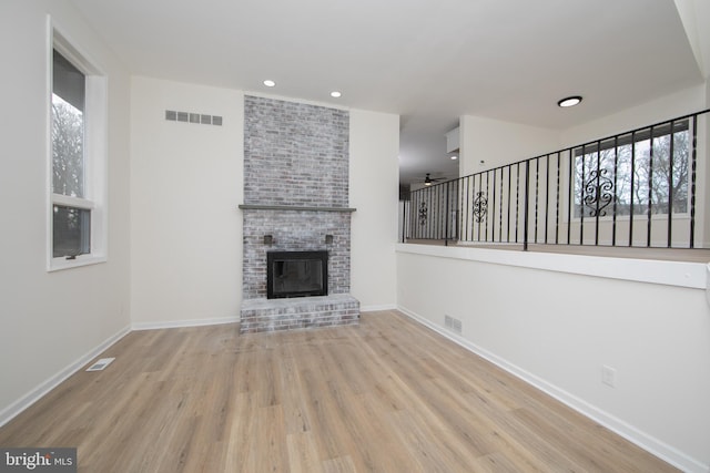 unfurnished living room featuring a brick fireplace, plenty of natural light, wood finished floors, and visible vents