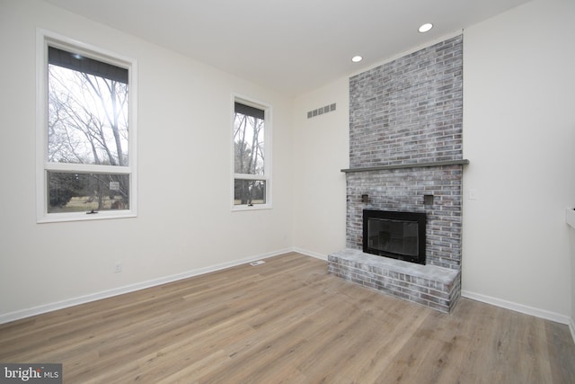 unfurnished living room featuring visible vents, a fireplace, baseboards, and wood finished floors