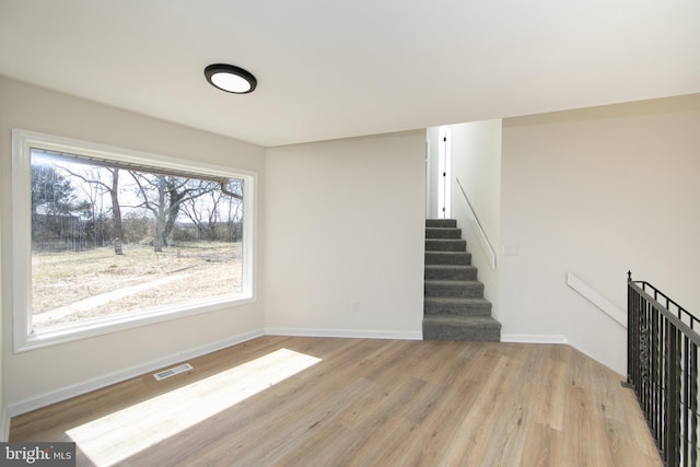 unfurnished living room featuring stairs, baseboards, visible vents, and light wood finished floors