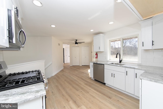 kitchen with tasteful backsplash, light wood-type flooring, white cabinets, stainless steel appliances, and a sink