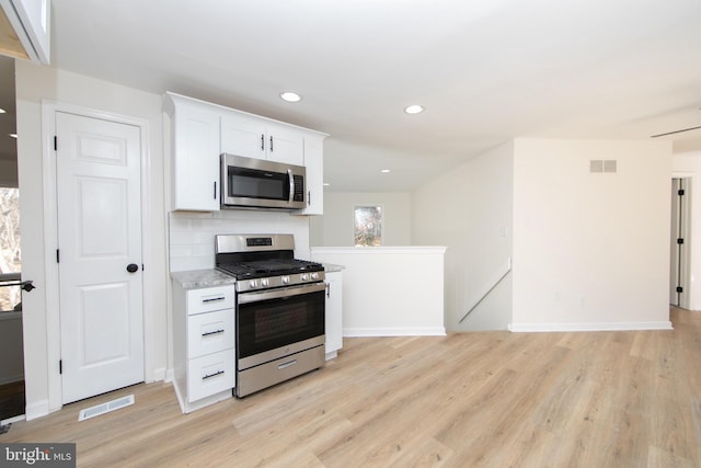 kitchen featuring visible vents, light wood-type flooring, decorative backsplash, appliances with stainless steel finishes, and white cabinets