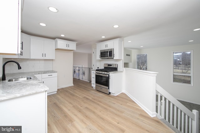 kitchen with a sink, white cabinets, light wood finished floors, and stainless steel appliances