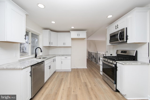 kitchen featuring light wood finished floors, light stone counters, white cabinets, stainless steel appliances, and a sink