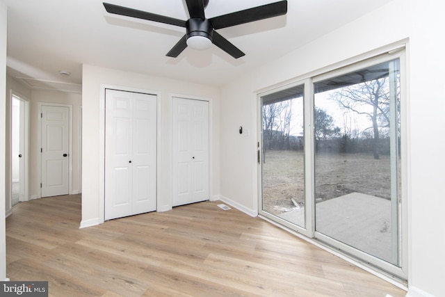 unfurnished bedroom featuring baseboards, multiple closets, light wood-style flooring, and access to outside