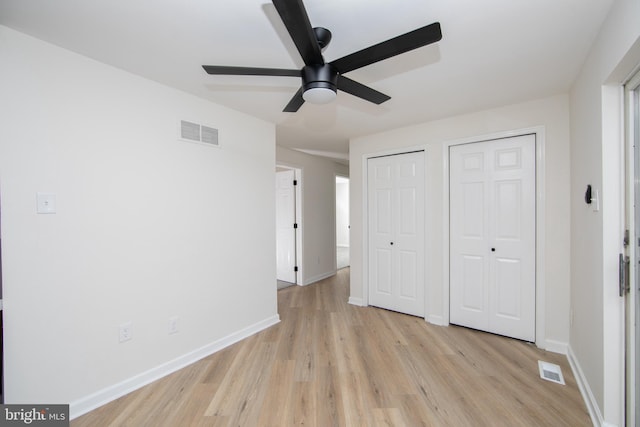 unfurnished bedroom with visible vents, baseboards, light wood-style floors, and multiple closets