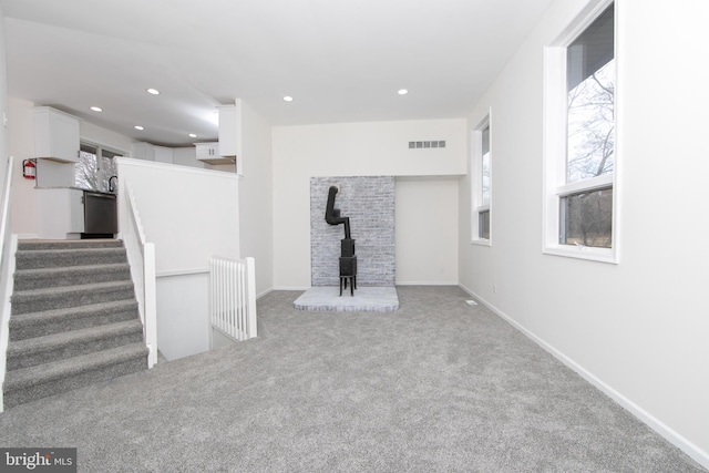 unfurnished living room featuring carpet flooring, a wood stove, plenty of natural light, and visible vents