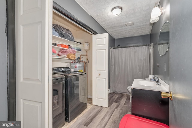 laundry room with wood finished floors, laundry area, a sink, a textured ceiling, and independent washer and dryer