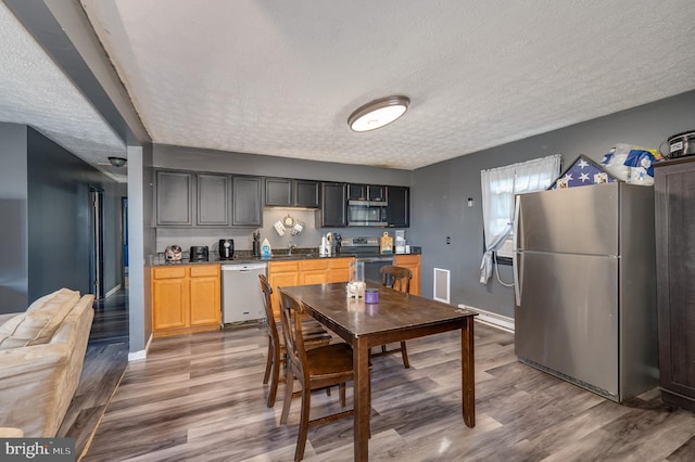 kitchen with wood finished floors, baseboards, appliances with stainless steel finishes, and a textured ceiling