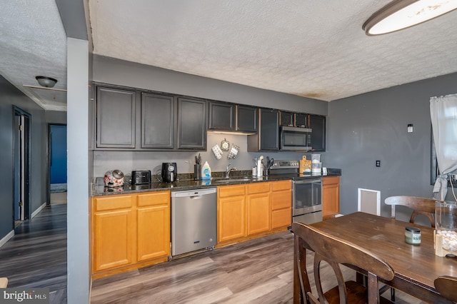 kitchen featuring a sink, a textured ceiling, appliances with stainless steel finishes, and wood finished floors