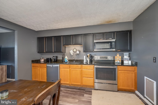 kitchen featuring a textured ceiling, light wood-style floors, appliances with stainless steel finishes, and a sink