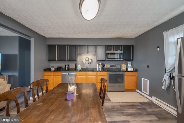 kitchen featuring dark countertops, baseboard heating, appliances with stainless steel finishes, wood finished floors, and a textured ceiling