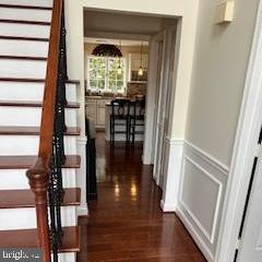 hallway with dark wood-type flooring, wainscoting, and a decorative wall