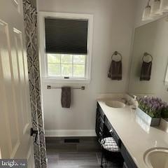 full bath featuring double vanity, wood finished floors, baseboards, and a sink