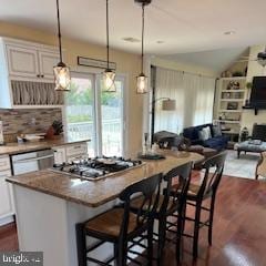 kitchen with a breakfast bar, a kitchen island, dark wood-style floors, stainless steel gas stovetop, and dishwasher