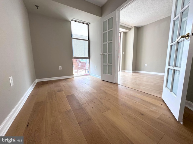 unfurnished room featuring french doors, baseboards, a textured ceiling, and light wood finished floors