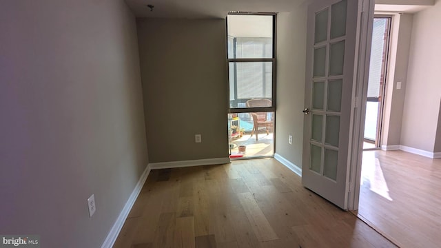 unfurnished room featuring a wall of windows, light wood-style flooring, and baseboards