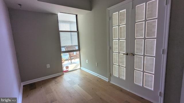 spare room with french doors, expansive windows, baseboards, and wood finished floors