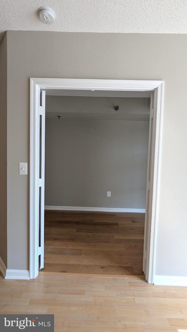 corridor with a textured ceiling, baseboards, and wood finished floors