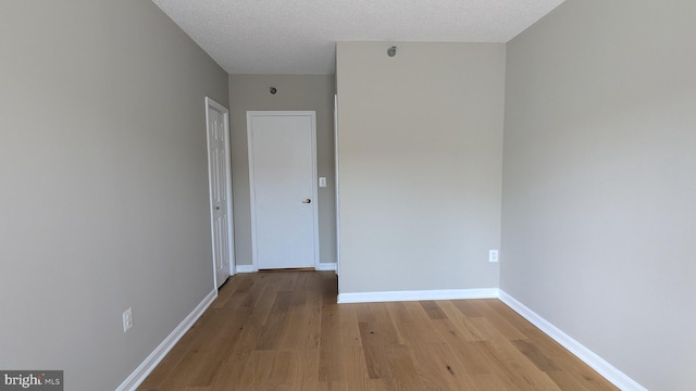 unfurnished room featuring baseboards, light wood-style floors, and a textured ceiling