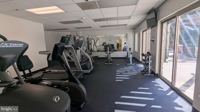 gym featuring a paneled ceiling and baseboards