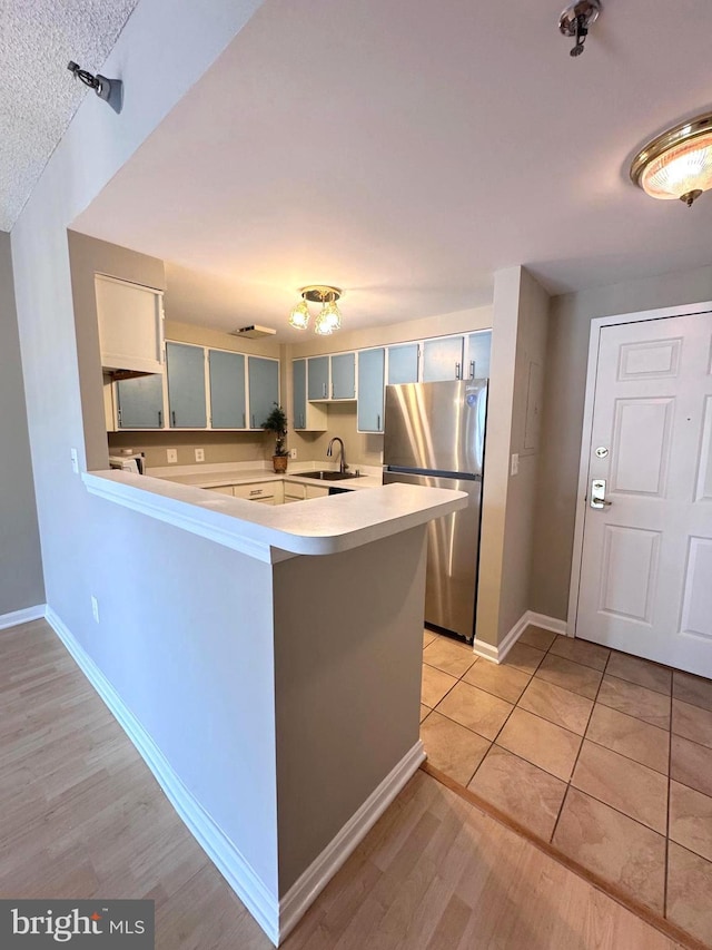 kitchen with light wood-style flooring, a sink, freestanding refrigerator, a peninsula, and light countertops