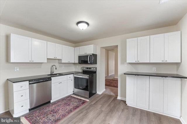 kitchen with a sink, stainless steel appliances, dark countertops, and white cabinetry