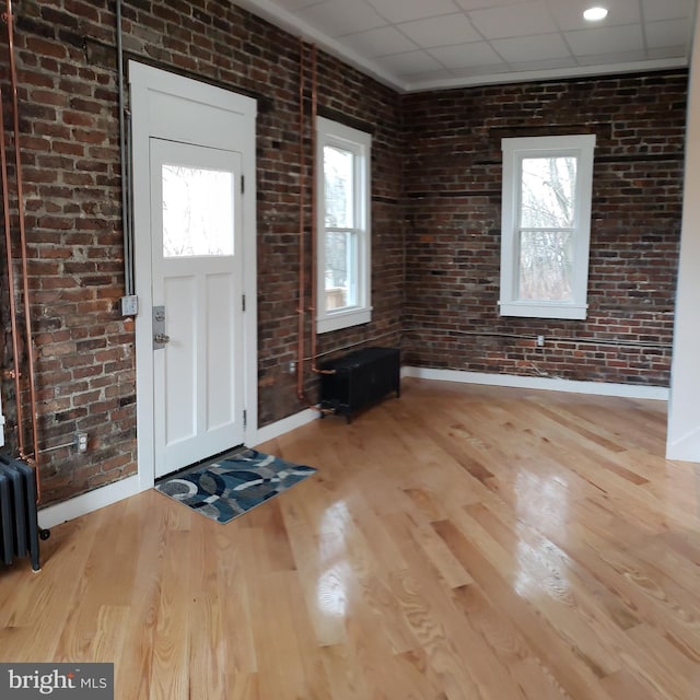 foyer featuring plenty of natural light, brick wall, a paneled ceiling, and wood finished floors