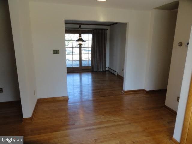 empty room featuring a baseboard heating unit, wood finished floors, and baseboards