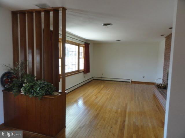 unfurnished living room featuring baseboard heating, visible vents, light wood-type flooring, and baseboards