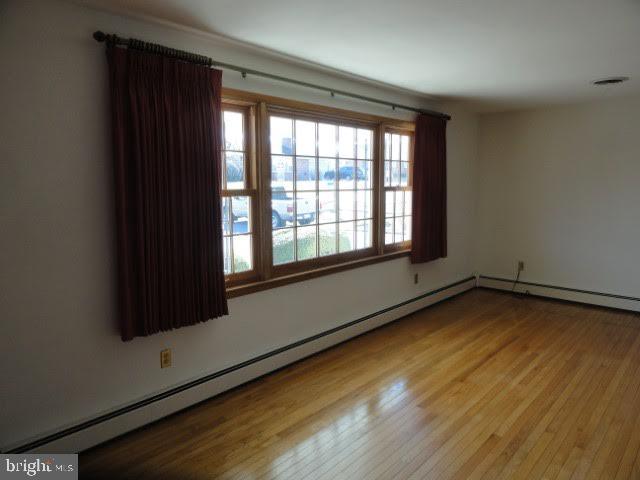 spare room with a baseboard heating unit, visible vents, and wood finished floors