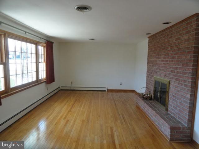 unfurnished living room with wood finished floors, visible vents, baseboards, a fireplace, and baseboard heating