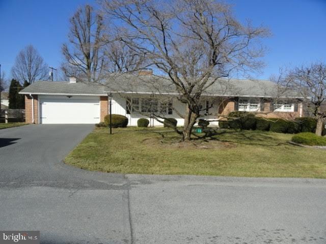 ranch-style house with aphalt driveway, an attached garage, a front yard, and a chimney