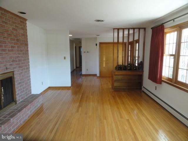 unfurnished living room featuring baseboard heating, a brick fireplace, baseboards, and wood finished floors