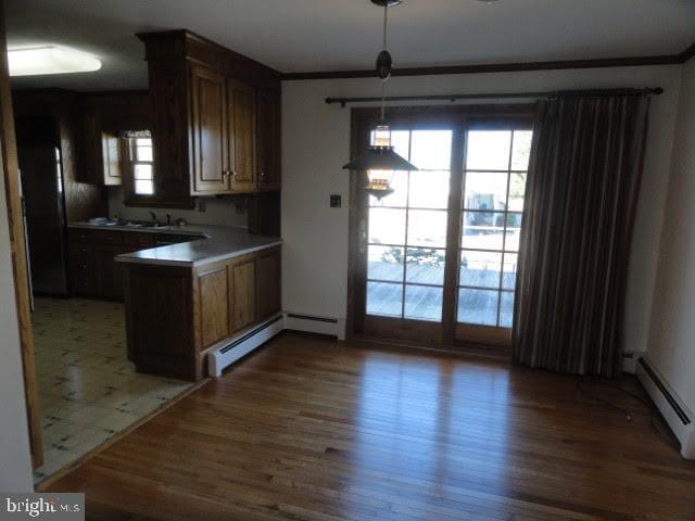 kitchen with decorative light fixtures, a peninsula, a baseboard heating unit, and wood finished floors