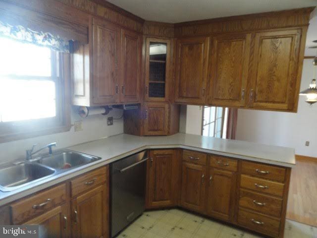 kitchen featuring brown cabinets, a sink, light countertops, dishwashing machine, and light floors