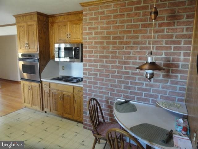 kitchen featuring brick wall, light floors, light countertops, brown cabinets, and appliances with stainless steel finishes