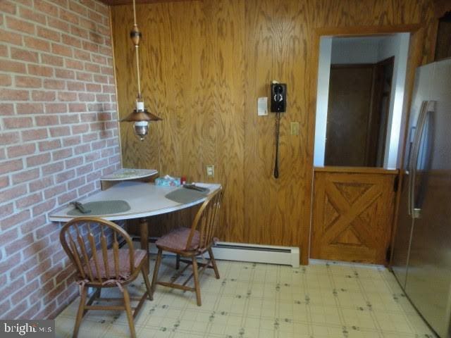 dining room with wooden walls, light floors, brick wall, and a baseboard heating unit