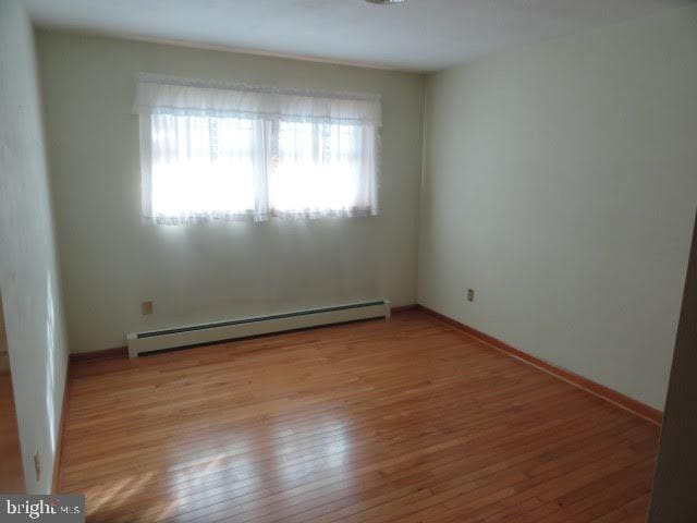 empty room featuring a baseboard radiator, baseboards, and wood finished floors