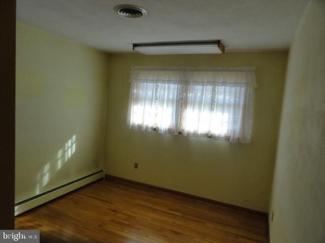 empty room featuring visible vents, wood finished floors, baseboards, and a baseboard radiator