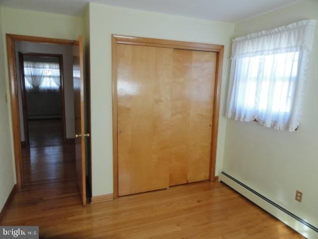 unfurnished bedroom featuring light wood-style floors, a closet, baseboard heating, and a baseboard radiator