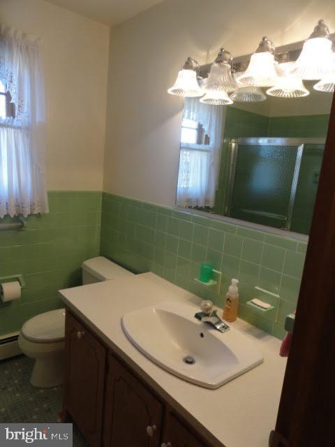 bathroom with an enclosed shower, toilet, tile walls, wainscoting, and vanity