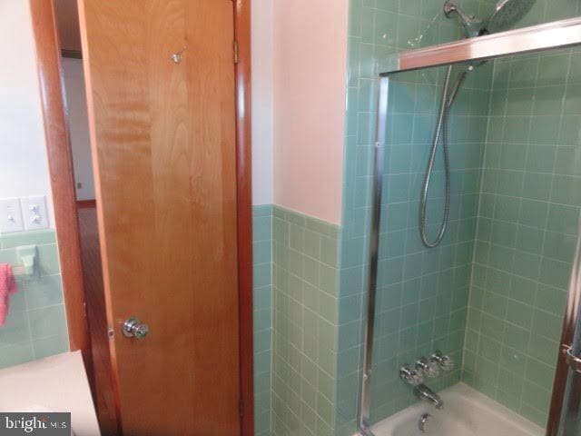 full bath with tile walls, washtub / shower combination, and a wainscoted wall