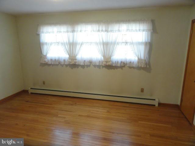 unfurnished bedroom with multiple windows, wood finished floors, and baseboard heating