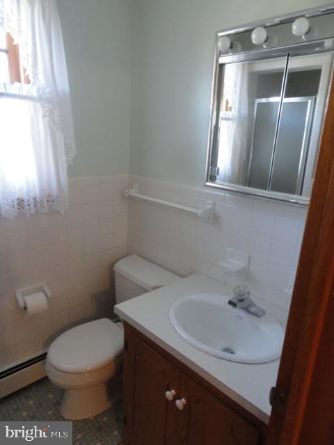 bathroom featuring vanity, a stall shower, tile walls, toilet, and baseboard heating