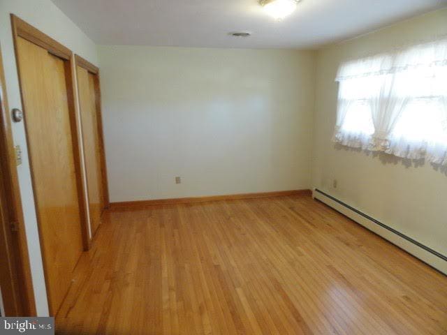 empty room featuring baseboards, light wood finished floors, and a baseboard radiator