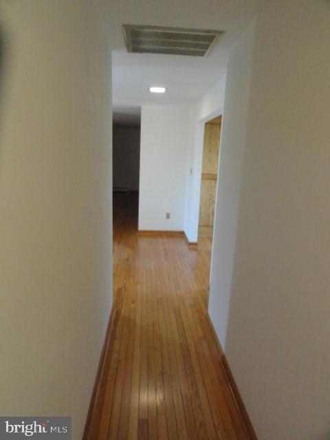 hall with visible vents, baseboards, and hardwood / wood-style flooring